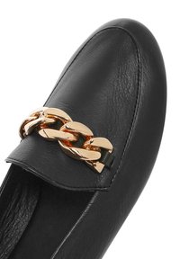 Mocassino in pelle nera con punta arrotondata e accentatura in catena dorata sul collo del piede, caratterizzato da una superficie liscia e dettagli di cucitura minimali.