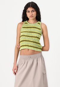 Top court en tricot vert clair avec des rayures vert foncé et jaunes. Doté d'un col rond et d'une finition texturée. Associé à une jupe beige.