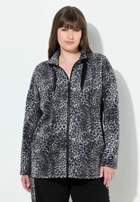 Veste zippée en imprimé léopard gris et noir avec un col, des poches latérales et des accents noirs contrastants le long de la fermeture éclair et des poignets. Texture douce.