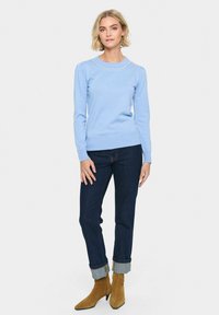 Maglione azzurro chiaro a maniche lunghe con scollatura rotonda e perle decorative. Abbinato a jeans scuri con orli arrotolati e stivali beige.