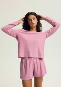 Jasnoróżowy zestaw odzieży dresowej z ribbowanej tkaniny, składający się z krótkiego, długiego rękawa oraz spodenek na elastycznej talii, charakteryzujący się miękką teksturą i luźnym krojem.