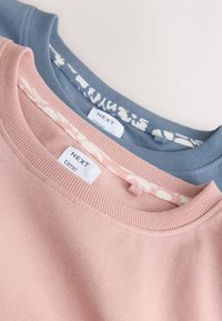 Deux sweat-shirts côtelés à col rond, un rose et un bleu, superposés avec des étiquettes NEXT time visibles et des cols intérieurs à motifs.