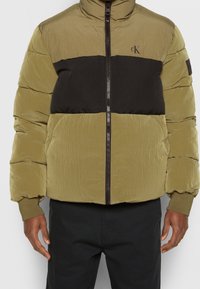 Calvin Klein puffjacka med en olivgrön och svart färgblockdesign, quiltad textur, hög krage och dragkedjestängning.