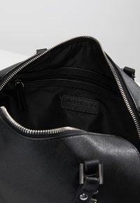 Svart läderhandväska med en öppen dragkedja, med en slät inredning och flera innerfickor. Inkluderar en varumärkesetikett inuti.