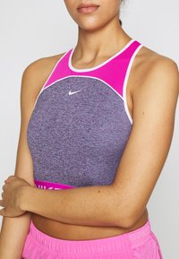 Haut court de sport violet avec un col en mesh rose et un bord blanc ; présente un petit logo Nike blanc à l'avant et une bande rose en bas.