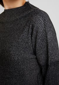 Maglione a coste nere con collo alto e un sottile luccichio metallico. Presenta motivi a righe orizzontali e verticali per aggiungere texture.
