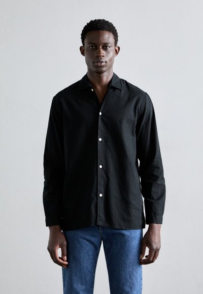 Camisa negra de manga larga con cuello, con botones blancos y una tela texturizada. Combinada con jeans de mezclilla azules.