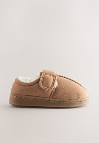 Chausson en daim marron avec doublure en polaire blanche et bride à boucle auto-agrippante réglable sur fond beige.