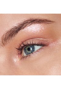 Gros plan sur un œil humain avec une paupière scintillante rose clair, des cils bien définis et un iris bleu avec un anneau intérieur jaune-brun.