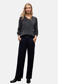 Harmaa neulepaita, jossa on V-pääntie ja pitkät hihat. Yhdistetty laajoihin tummansinisiin housuihin ja mustiin kenkiin. Yksinkertainen muotoilu, ei näkyviä kuvioita.