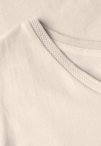 Ljusbeige T-shirt med en strukturerad rund halsringning, mjuk bomullstyg och en enkel, odekorerad design.