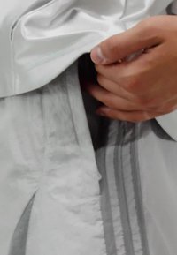 Tessuto grigio leggero e texturizzato con finitura satinata. Presenta una cerniera nascosta e un design a strati. Regolazione manuale della vestibilità del capo.