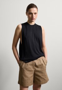 Schwarzes ärmelloses Oberteil mit Rundhalsausschnitt, kombiniert mit beigefarbenen Leinen-Shorts mit Vorderfalten und seitlichen Taschen. Glatte Stofftextur.