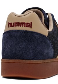 Blå mocka och texturerade tygsneakers med beige detaljer, som har en brun gummisul och broderad "hummel"-logotyp på hälen.