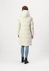 Light beige puffer coat with horizontal stitching, large hood, and knee-length design, paired with blue jeans and black ankle boots.