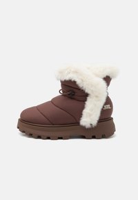 Brune isolerte ankelstøvler med en tykk hvit pelskrage, quiltet design, flat gummisåle og snøring på siden for justering.