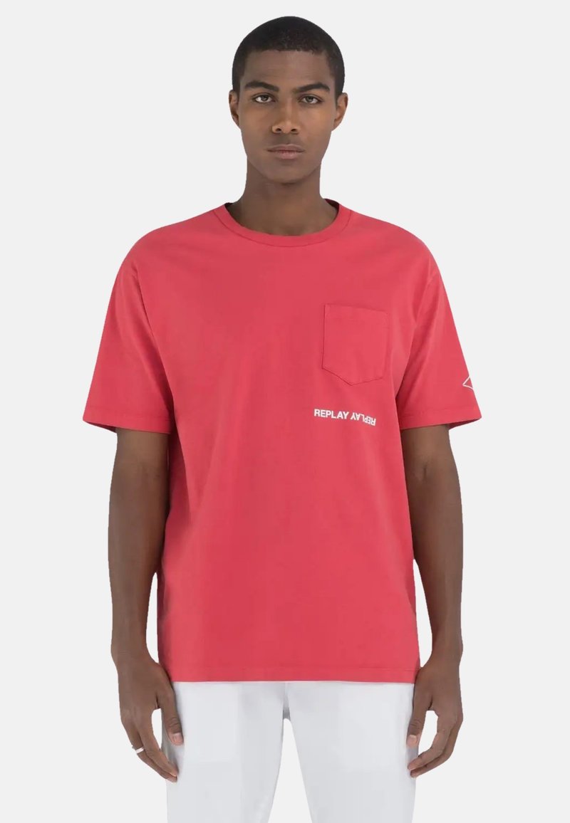 Rød bomulds t-shirt med korte ærmer, rund hals, frontlomme og et hvidt "REPLAY" logo nederst til venstre. Glat tekstur, afslappet pasform.