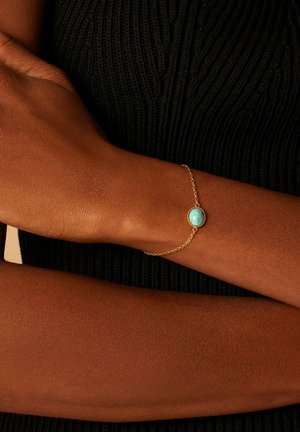 Goldarmband mit einem ovalen Türkisstein, versehen mit einer zarten Kette. Das Design ist minimalistisch mit einem glatten Stein und feinen Gliedern.