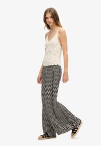 Top de punto blanco sin mangas con escote en V, combinado con pantalones de pierna ancha de patrón blanco y negro. Sandalias negras completan el look.