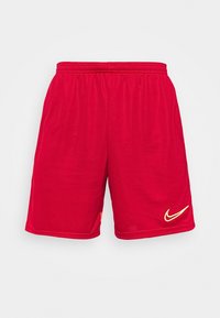 Shorts de sport rouges en matériau léger. Ils disposent d'une taille élastique et d'un logo Swoosh jaune de Nike en bas à droite.