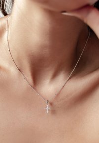 Zilveren ketting met een hanger in de vorm van een kruis, versierd met kleine decoratieve steentjes, rustend op de huid.