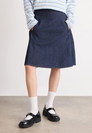 D mørkeblå denim A-linje skjørt med sidelommer og rå kant. Kombinert med svarte Mary Jane-sko og hvite ribbestrikkede sokker.