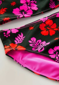Bikini nero con vivaci motivi floreali in rosa e rosso, caratterizzato da un tessuto morbido, una fodera rosa a contrasto e dettagli di cucitura visibili.