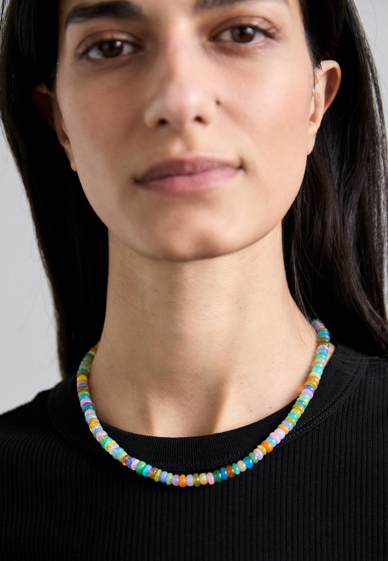 Värviline helmestest kaelakee, mis koosneb ümmargustest mitmevärvilistest klaashelmestest erinevates suurustes, kandjaks on musta soonilise topiga inimene.