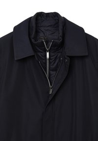 Cappotto blu navy con una sovrastruttura interna trapuntata staccabile, chiusura con zip, colletto flat e una leggera lucentezza. Presenta dettagli in argento per la zip e i bottoni.