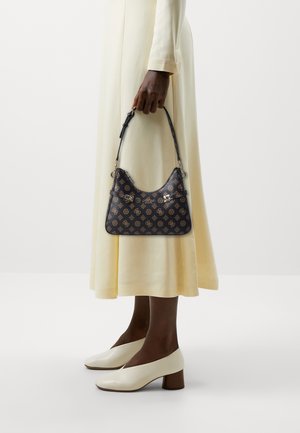 Schwarze, gemusterte Handtasche mit geschwungener Form, ausgestattet mit einem kurzen Riemen und silbernen Beschlägen, gehalten von einer Person in einem langen, hellgelben Kleid.