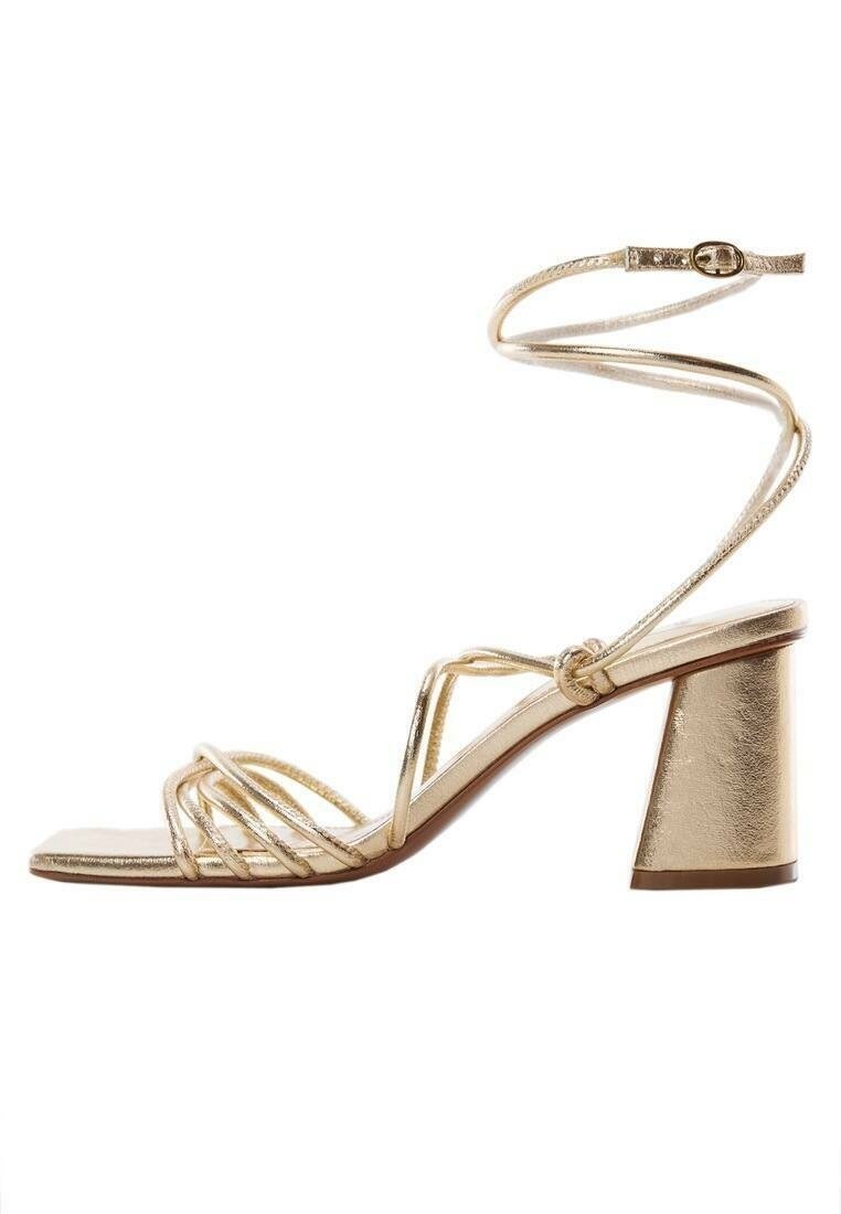 Sandales à talons métalliques dorées avec un orteil carré, un design à plusieurs straps et un talon bloc chunky. Fine lanière à la cheville avec détail de boucle ajustable.