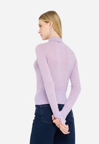 Top lungo a maniche lunghe di colore viola chiaro con design aderente, colletto alto e texture sottile. La vista posteriore mostra una costruzione senza cuciture e un piccolo dettaglio hardware.