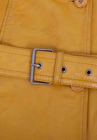 Gelber Ledergürtel mit einer silbernen Metallschließe. Merkmale sind sichtbare Nähte, eine glatte Textur und mehrere Einstelllöcher.