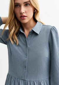 Light blue button-up dress with a textured fabric, collar, and puff sleeves. Features a gathered skirt and matching buttons.