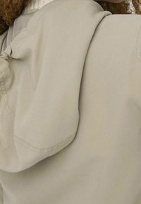 Beige jacket featuring a hood, with a smooth texture, soft fabric, and gathered detail on the shoulder seam.
