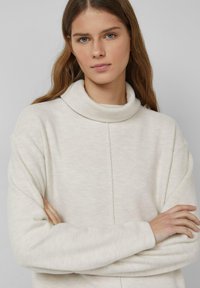 Jasnobeżowy sweter z golfem wykonany z miękkiego, teksturowanego materiału. Charakteryzuje się luźnym krojem, długimi rękawami oraz prostym, czystym designem.