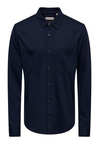 Marineblå knappeskjorte laget av teksturert stoff med spredt krage, to brystlommer og buet nederkant.
