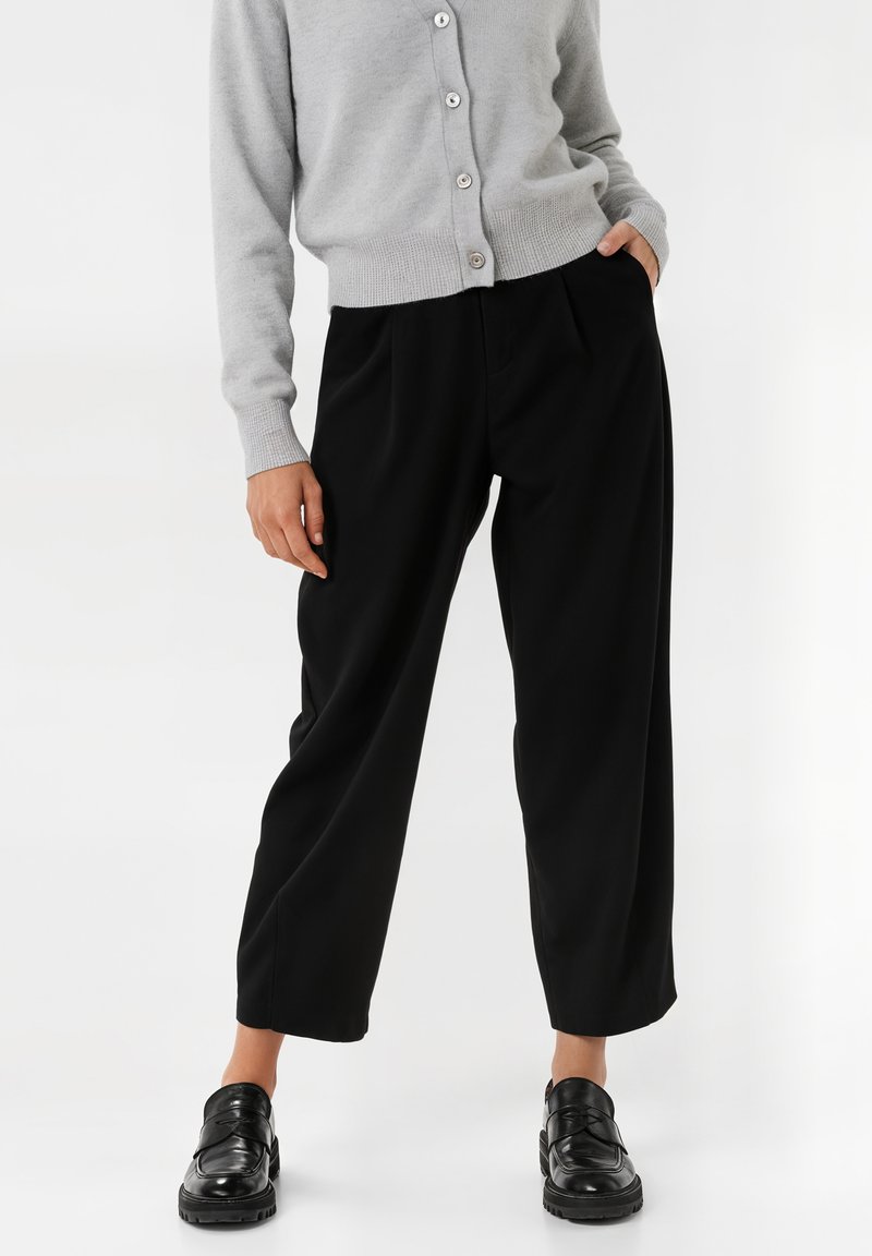 Black pleated trousers with a relaxed fit, made of smooth fabric. Paired with a light gray cardigan featuring buttons and ribbed cuffs.