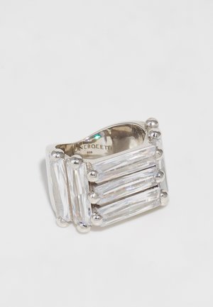Bague en argent avec trois grandes pierres rectangulaires transparentes disposées horizontalement, accompagnées de accents en métal arrondis à chaque extrémité. Fini poli.