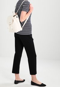 Vit läderryggsäck med klaffstängning och dragsko, bärs över ena axeln. Tillsammans med en randig skjorta och svarta cropped byxor.