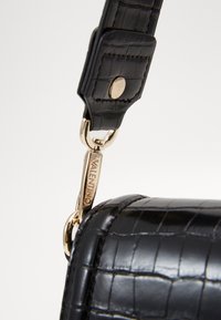 Black faux leather bag strap with crocodile texture, featuring a gold-tone metal clip and branded hardware.