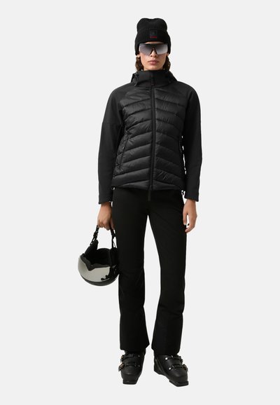 Černá nadýchaná bunda s elastickým střihem a zipovým zapínáním, doplněná černými kalhotami a botami. Doplňky zahrnují černou čepici a zrcadlovou helmu.