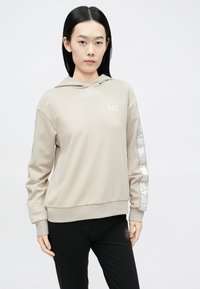 Bēša kapuce ar garām piedurknēm, uz krūtīm logotips un atstarojoša svītra uz piedurknes. Gluda auduma faktūra.