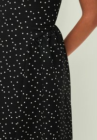 Black dress with white polka dots, featuring a fitted bodice, gathered waist, and smooth texture. Side pocket detail visible.