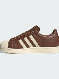 Καφέ δερμάτινο παπούτσι τύπου low-top με κρεμ χρωματισμένη γόμα στη μύτη, κρεμ σόλα και τρεις κρεμ ρίγες στο πλάι, δεμένο με καφέ κορδόνια.