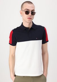 Polo skjorte med marineblå topp, røde ermer og hvitt nederste parti. Laget av bomull med klassisk krage og knapper.