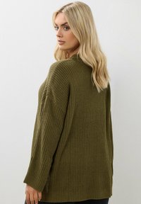 Oliwkowy sweter dzianinowy o luźnym kroju, teksturowany materiał i boczne rozcięcia. Posiada długie rękawy i wysoki dekolt.