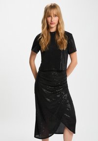 Completo due pezzi nero con paillettes, composto da un top corto con maniche corte e una gonna aderente arricciata con design avvolgente.