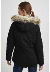 Zwarte jas met een zachte, faux fur capuchon trim. Beschikt over een trekkoord in de taille, een capuchon en een effen, gestructureerde stof in een relaxte pasvorm.