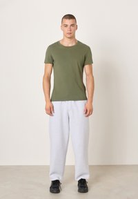 Alyvuogių žalios spalvos medvilniniai marškinėliai, derinami su šviesiai pilkomis sportinėmis kelnėmis. Apranga užbaigiama juodais sportiniais batais. Paprastas, kasdienis dizainas.